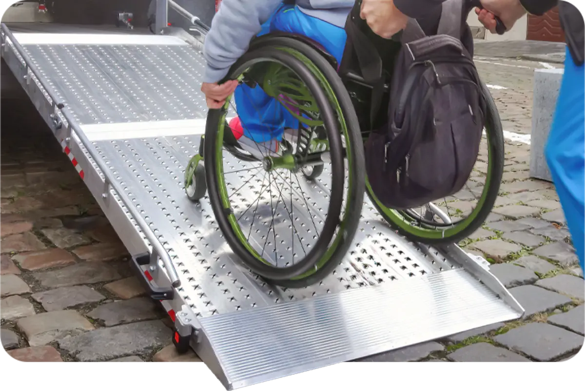 Individual in a wheelchair being wheeled up a metal wheelchair ramp